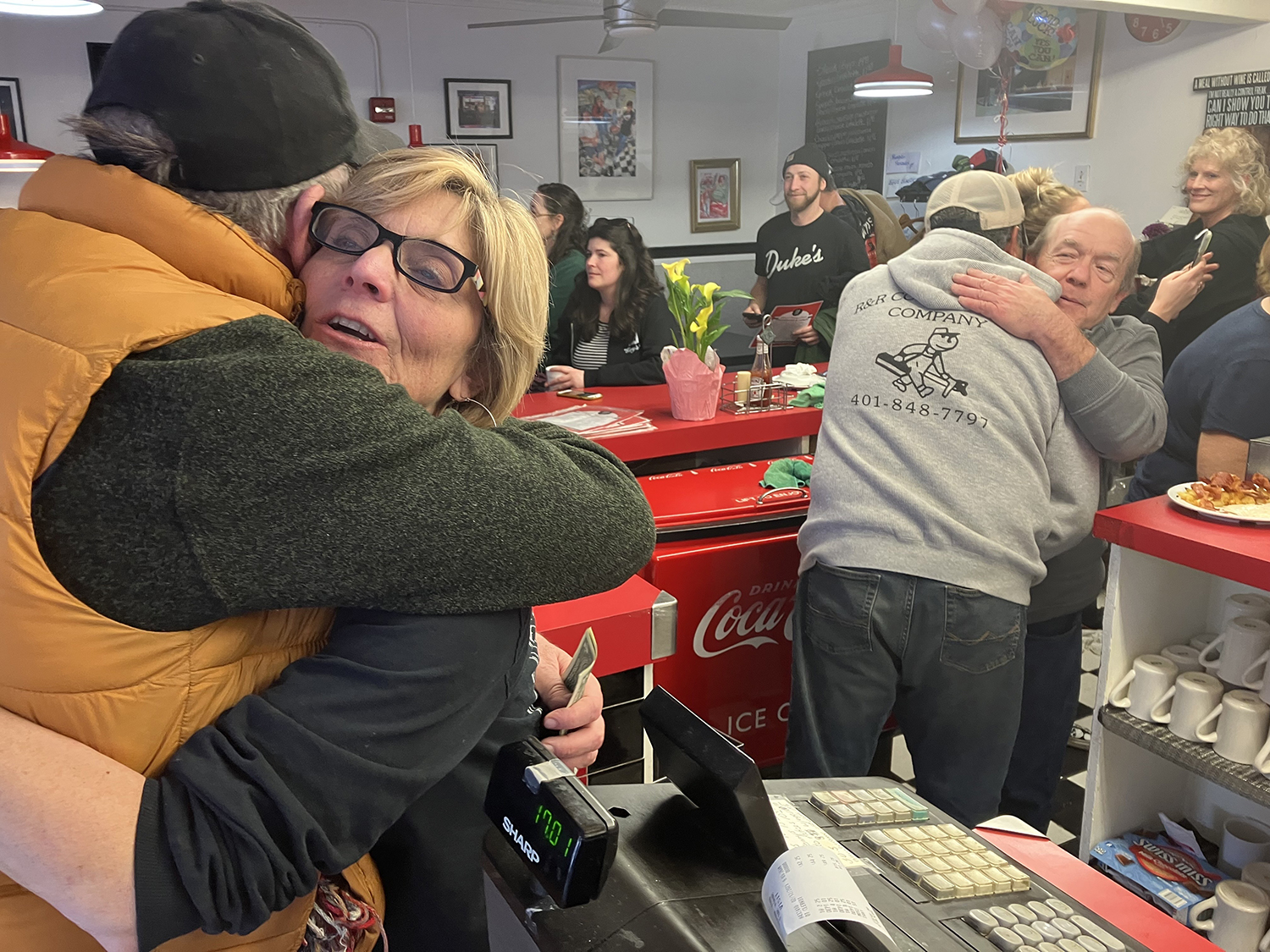 Tina DuBreuil, second from left, hugs a customer as her brother, Joel Richards, back right, hugs another customer at Gary's Handy Lunch. The beloved family diner closed its doors on Feb. 12, 2023, in Newport, RI. DuBreuil has worked at the restaurant for nearly 40 years; Richards has worked there since he was a teen.
