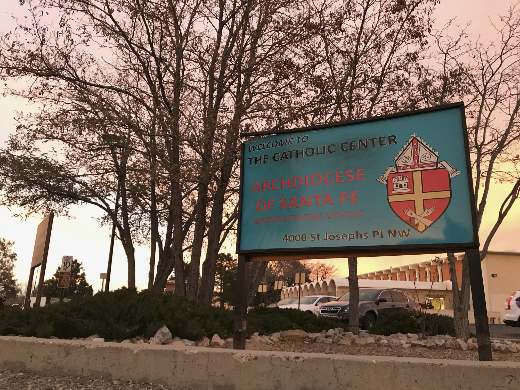 FILE - In this Nov. 29, 2018, file photo, the sun sets on a sign in front of the Archdiocese of Santa Fe offices in Albuquerque, N.M. A priest who fled the United States decades ago faces a federal trial on charges that he sexually abused a New Mexico boy in the early 1990s at an Air Force base and veterans' cemetery. Arthur Perrault, a one-time pastor in Albuquerque, has been charged with aggravated sexual abuse and others counts. (AP Photo/Susan Montoya Bryan, File) FILE - In this Nov. 29, 2018, file photo, the sun sets on a sign in front of the Archdiocese of Santa Fe offices in Albuquerque, N.M. A priest who fled the United States decades ago faces a federal trial on charges that he sexually abused a New Mexico boy in the early 1990s at an Air Force base and veterans' cemetery. Arthur Perrault, a one-time pastor in Albuquerque, has been charged with aggravated sexual abuse and others counts. (AP Photo/Susan Montoya Bryan, File)