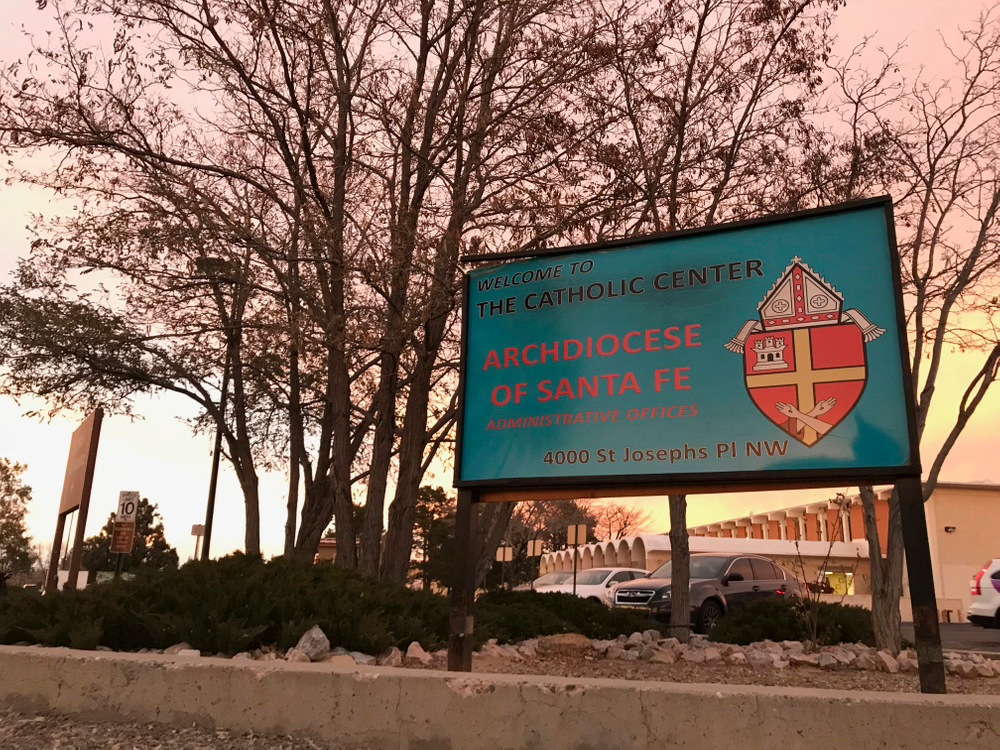 FILE - In this Nov. 29, 2018, file photo, the sun sets on a sign in front of the Archdiocese of Santa Fe offices in Albuquerque, N.M. A priest who fled the United States decades ago faces a federal trial on charges that he sexually abused a New Mexico boy in the early 1990s at an Air Force base and veterans' cemetery. Arthur Perrault, a one-time pastor in Albuquerque, has been charged with aggravated sexual abuse and others counts. (AP Photo/Susan Montoya Bryan, File) FILE - In this Nov. 29, 2018, file photo, the sun sets on a sign in front of the Archdiocese of Santa Fe offices in Albuquerque, N.M. A priest who fled the United States decades ago faces a federal trial on charges that he sexually abused a New Mexico boy in the early 1990s at an Air Force base and veterans' cemetery. Arthur Perrault, a one-time pastor in Albuquerque, has been charged with aggravated sexual abuse and others counts. (AP Photo/Susan Montoya Bryan, File)