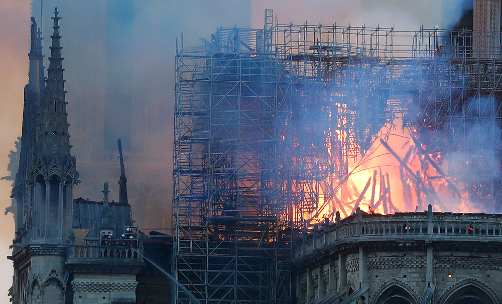 Firefighters tackle the blaze as flames and smoke rise from Notre Dame cathedral as it burns in Paris, Monday, April 15, 2019. Massive plumes of yellow brown smoke is filling the air above Notre Dame Cathedral and ash is falling on tourists and others around the island that marks the center of Paris. (AP Photo/Thibault Camus) Firefighters tackle the blaze as flames and smoke rise from Notre Dame cathedral as it burns in Paris, Monday, April 15, 2019. Massive plumes of yellow brown smoke is filling the air above Notre Dame Cathedral and ash is falling on tourists and others around the island that marks the center of Paris. (AP Photo/Thibault Camus)