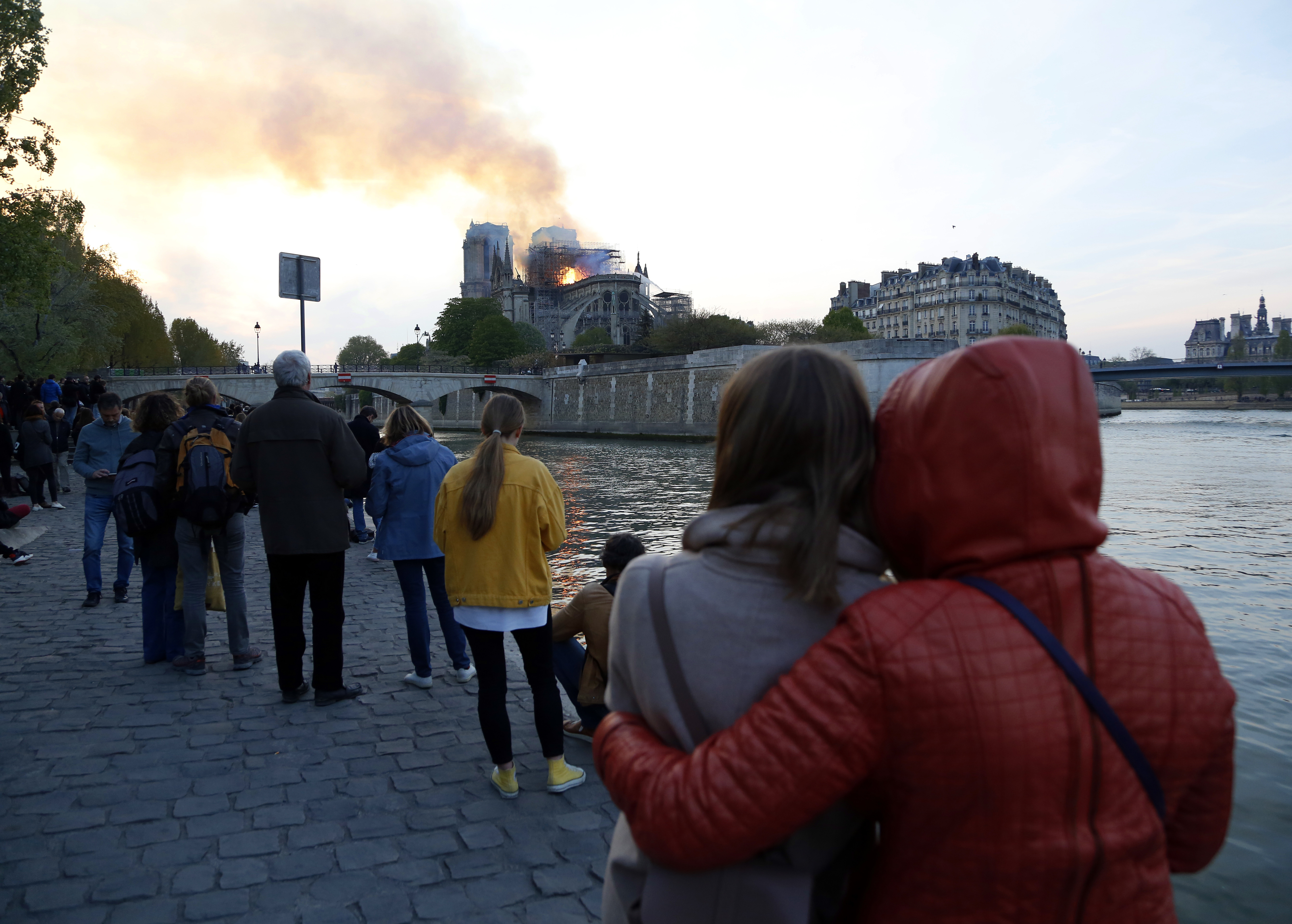 People watch as flames and smoke rise from Notre Dame cathedral as it burns in Paris, Monday, April 15, 2019. Massive plumes of yellow brown smoke is filling the air above Notre Dame Cathedral and ash is falling on tourists and others around the island that marks the center of Paris. (AP Photo/Thibault Camus) People watch as flames and smoke rise from Notre Dame cathedral as it burns in Paris, Monday, April 15, 2019. Massive plumes of yellow brown smoke is filling the air above Notre Dame Cathedral and ash is falling on tourists and others around the island that marks the center of Paris. (AP Photo/Thibault Camus)