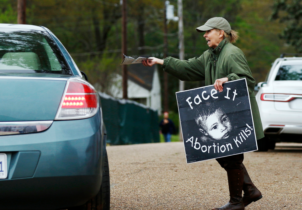 FILE - In this March 20, 2018, file photo, anti-abortion sidewalk counselor Laura Duran, offers reading material to a driver entering the Jackson Women's Health Organization's clinic, the only facility in the state that performs abortions, in Jackson, Miss. As abortion opponents cheer the passage of fetal heartbeat laws such as the one in Mississippi and other restrictions on the procedure, abortion-rights groups have been waging a quieter battle in courthouses around the country to overturn limits on providers. (AP Photo/Rogelio V. Solis, File) FILE - In this March 20, 2018, file photo, anti-abortion sidewalk counselor Laura Duran, offers reading material to a driver entering the Jackson Women's Health Organization's clinic, the only facility in the state that performs abortions, in Jackson, Miss. As abortion opponents cheer the passage of fetal heartbeat laws such as the one in Mississippi and other restrictions on the procedure, abortion-rights groups have been waging a quieter battle in courthouses around the country to overturn limits on providers. (AP Photo/Rogelio V. Solis, File)