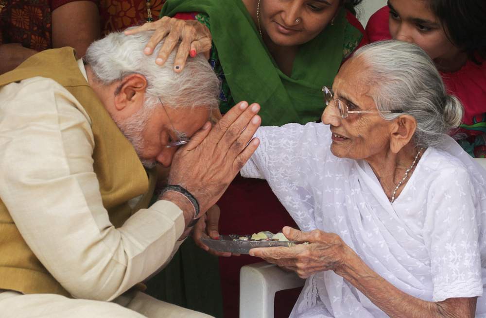 FILE - In this May 16, 2014 file photo, 90-year-old Hiraben blesses her son and India's next prime minister Narendra Modi at her home in Gandhinagar, in the western Indian state of Gujarat. Indian Prime Minister Narendra Modi's party claimed it had won re-election with a commanding lead in vote count Thursday, May 23, 2019. Modi was the third of six children born to Damodardas Modi, who ran a small tea shop at the local railway station in the tiny town of Vadnagar, in the western state of Gujarat. The family struggled to make ends meet, which meant Modi had to help his father run the shop. Modi began his political rise as a teenager in Gujarat, joining the militant Hindu organization Rashtriya Swayamsewak Sangh, which modeled itself in the 1930s after fascist Italy and which is regarded as the ideological parent of the BJP. (AP Photo/Ajit Solanki, File) FILE - In this May 16, 2014 file photo, 90-year-old Hiraben blesses her son and India's next prime minister Narendra Modi at her home in Gandhinagar, in the western Indian state of Gujarat. Indian Prime Minister Narendra Modi's party claimed it had won re-election with a commanding lead in vote count Thursday, May 23, 2019. Modi was the third of six children born to Damodardas Modi, who ran a small tea shop at the local railway station in the tiny town of Vadnagar, in the western state of Gujarat. The family struggled to make ends meet, which meant Modi had to help his father run the shop. Modi began his political rise as a teenager in Gujarat, joining the militant Hindu organization Rashtriya Swayamsewak Sangh, which modeled itself in the 1930s after fascist Italy and which is regarded as the ideological parent of the BJP. (AP Photo/Ajit Solanki, File)
