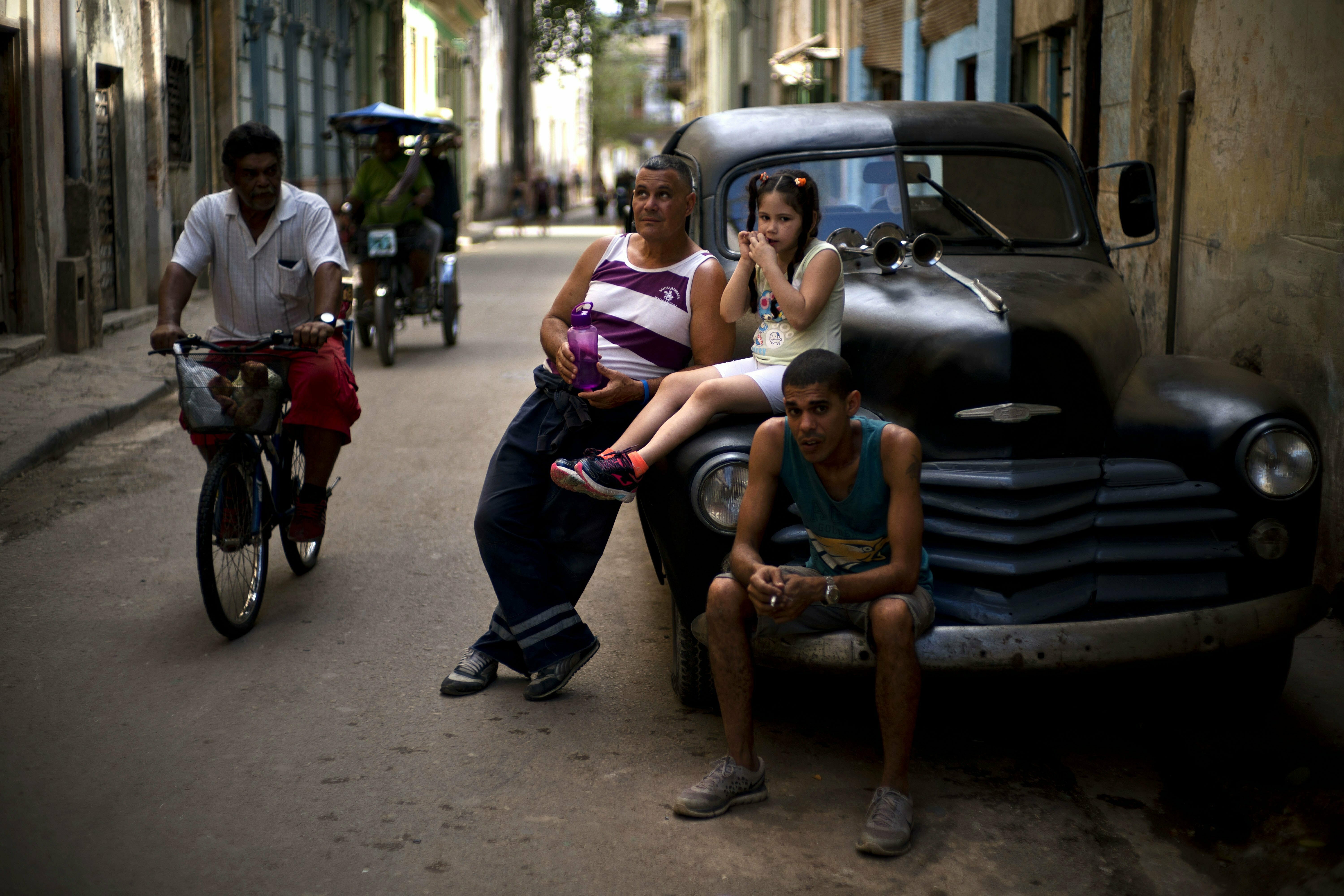 People rest on a classic American car as a man pedals his bike past in Havana, Cuba, Wednesday, April 10, 2019. Communist Party leader Raúl Castro warned Cubans on Wednesday that they should brace for worsening shortages due to Trump administration policies, but said the island won't return to the extreme deprivation of the post-Soviet period. (AP Photo/Ramon Espinosa) People rest on a classic American car as a man pedals his bike past in Havana, Cuba, Wednesday, April 10, 2019. Communist Party leader Raúl Castro warned Cubans on Wednesday that they should brace for worsening shortages due to Trump administration policies, but said the island won't return to the extreme deprivation of the post-Soviet period. (AP Photo/Ramon Espinosa)