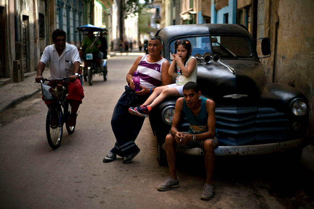 People rest on a classic American car as a man pedals his bike past in Havana, Cuba, Wednesday, April 10, 2019. Communist Party leader Raúl Castro warned Cubans on Wednesday that they should brace for worsening shortages due to Trump administration policies, but said the island won't return to the extreme deprivation of the post-Soviet period. (AP Photo/Ramon Espinosa) People rest on a classic American car as a man pedals his bike past in Havana, Cuba, Wednesday, April 10, 2019. Communist Party leader Raúl Castro warned Cubans on Wednesday that they should brace for worsening shortages due to Trump administration policies, but said the island won't return to the extreme deprivation of the post-Soviet period. (AP Photo/Ramon Espinosa)