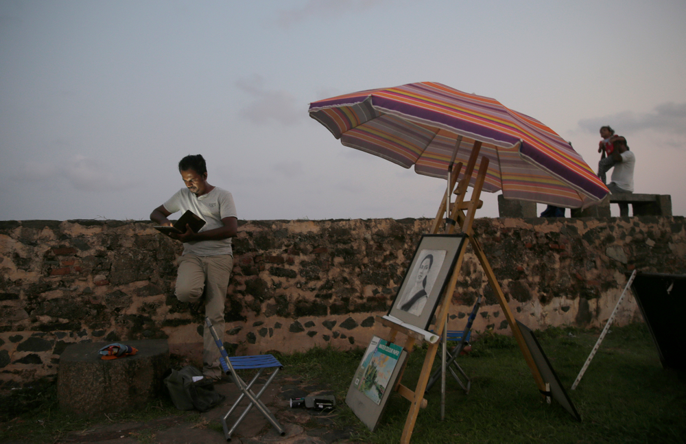 In this Friday, May 10, 2019, photo, a Sri Lankan street painter looks at his mobile phone as locals stand along the 17th century Dutch built rampart of the Galle fort in Galle, Sri Lanka. Sri Lanka was the Lonely Planet guide’s top travel destination for 2019, but since the Easter Sunday attacks on churches and luxury hotels, foreign tourists have fled. More than 250 people, including 45 foreigners mainly from China, India, the U.S. and the U.K., died in the Islamic State group-claimed blasts. (AP Photo/Eranga Jayawardena) In this Friday, May 10, 2019, photo, a Sri Lankan street painter looks at his mobile phone as locals stand along the 17th century Dutch built rampart of the Galle fort in Galle, Sri Lanka. Sri Lanka was the Lonely Planet guide’s top travel destination for 2019, but since the Easter Sunday attacks on churches and luxury hotels, foreign tourists have fled. More than 250 people, including 45 foreigners mainly from China, India, the U.S. and the U.K., died in the Islamic State group-claimed blasts. (AP Photo/Eranga Jayawardena)