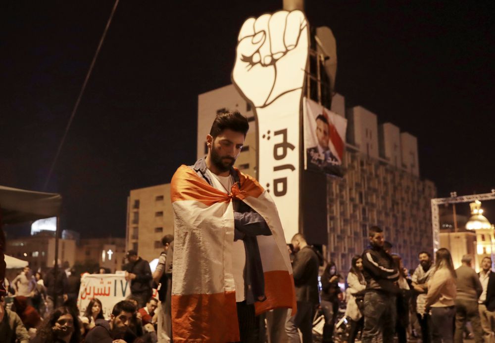 Anti-government protesters listen to the Lebanese President Michel Aoun as he delivers a televised speech on the eve of the country's 76th Independence Day, in downtown Beirut, Lebanon, Thursday, Nov. 21, 2019. Aoun barely mentioned the month-long protests in his speech and said consensus on government formation remained far off because of Anti-government protesters listen to the Lebanese President Michel Aoun as he delivers a televised speech on the eve of the country's 76th Independence Day, in downtown Beirut, Lebanon, Thursday, Nov. 21, 2019. Aoun barely mentioned the month-long protests in his speech and said consensus on government formation remained far off because of