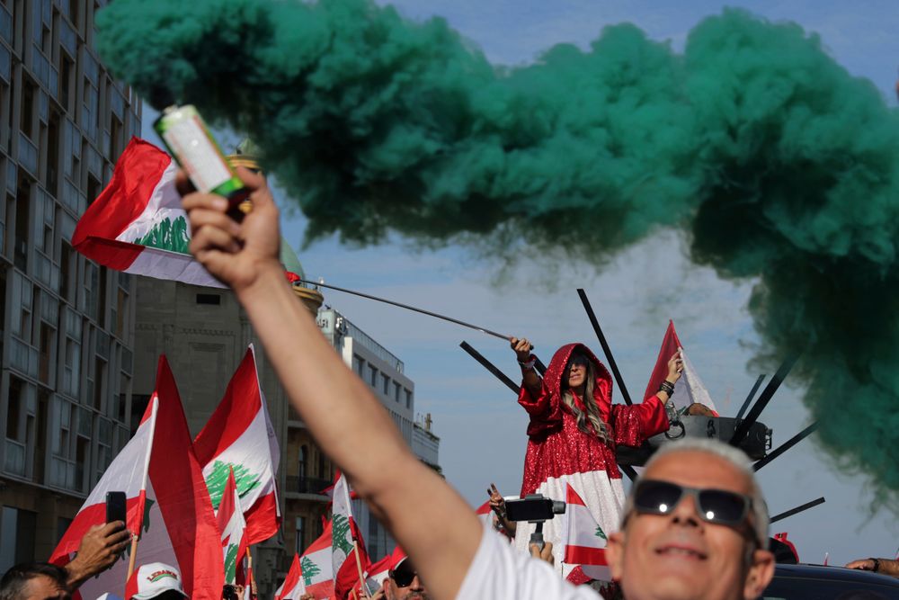Anti-government protesters wave Lebanese national flags as hold smoke flares during separate civil parade at the Martyr square, in downtown Beirut, Lebanon, Friday, Nov. 22, 2019. Protesters gathered for alternative independence celebrations, converging by early afternoon on Martyrs’ Square in central Beirut, which used to be the traditional location of the official parade. Protesters have occupied the area, closing it off to traffic since mid-October. (AP Photo/Hassan Ammar) Anti-government protesters wave Lebanese national flags as hold smoke flares during separate civil parade at the Martyr square, in downtown Beirut, Lebanon, Friday, Nov. 22, 2019. Protesters gathered for alternative independence celebrations, converging by early afternoon on Martyrs’ Square in central Beirut, which used to be the traditional location of the official parade. Protesters have occupied the area, closing it off to traffic since mid-October. (AP Photo/Hassan Ammar)