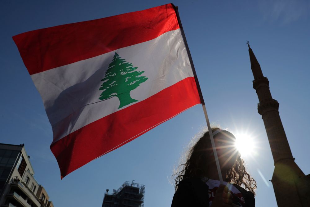 An anti-government protester holds the Lebanese national flag during separate civil parade at the Martyr square, in downtown Beirut, Lebanon, Friday, Nov. 22, 2019. Protesters gathered for their own alternative independence celebrations, converging by early afternoon on Martyrs' square in central Beirut, which used to be the traditional location for the official parade. Protesters have occupied the area, closing it off to traffic since mid-October. (AP Photo/Hassan Ammar) An anti-government protester holds the Lebanese national flag during separate civil parade at the Martyr square, in downtown Beirut, Lebanon, Friday, Nov. 22, 2019. Protesters gathered for their own alternative independence celebrations, converging by early afternoon on Martyrs' square in central Beirut, which used to be the traditional location for the official parade. Protesters have occupied the area, closing it off to traffic since mid-October. (AP Photo/Hassan Ammar)