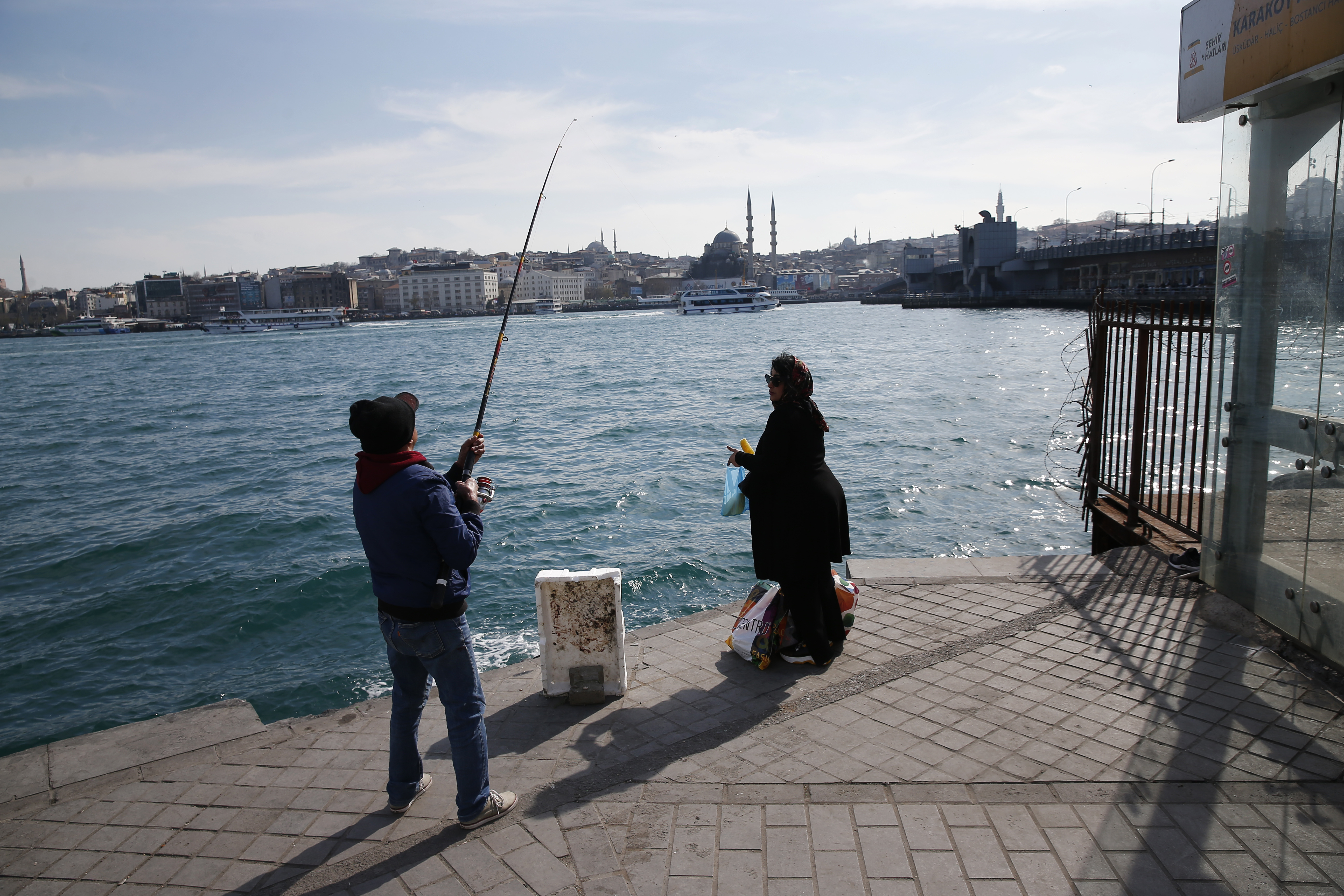 In this Thursday, April 4, 2019 photo, a man fishes at the Golden Horn as a woman waits for the boat to cross the Bosporus Strait from Europe to Asia, in Istanbul. The mood among opposition supporters in Turkey's biggest city is one of jubilation but also worry - fear that their win in Istanbul's mayoral race could be overturned in a recount taking place after the ruling party challenged the election results. (AP Photo/Lefteris Pitarakis) In this Thursday, April 4, 2019 photo, a man fishes at the Golden Horn as a woman waits for the boat to cross the Bosporus Strait from Europe to Asia, in Istanbul. The mood among opposition supporters in Turkey's biggest city is one of jubilation but also worry - fear that their win in Istanbul's mayoral race could be overturned in a recount taking place after the ruling party challenged the election results. (AP Photo/Lefteris Pitarakis)
