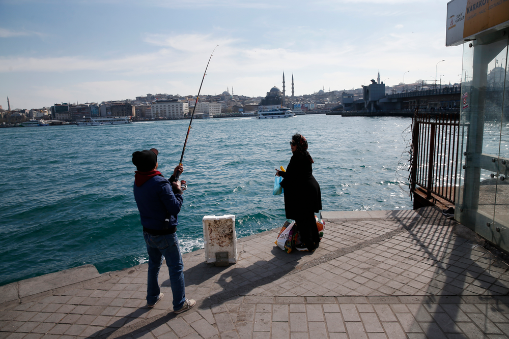 In this Thursday, April 4, 2019 photo, a man fishes at the Golden Horn as a woman waits for the boat to cross the Bosporus Strait from Europe to Asia, in Istanbul. The mood among opposition supporters in Turkey's biggest city is one of jubilation but also worry - fear that their win in Istanbul's mayoral race could be overturned in a recount taking place after the ruling party challenged the election results. (AP Photo/Lefteris Pitarakis) In this Thursday, April 4, 2019 photo, a man fishes at the Golden Horn as a woman waits for the boat to cross the Bosporus Strait from Europe to Asia, in Istanbul. The mood among opposition supporters in Turkey's biggest city is one of jubilation but also worry - fear that their win in Istanbul's mayoral race could be overturned in a recount taking place after the ruling party challenged the election results. (AP Photo/Lefteris Pitarakis)