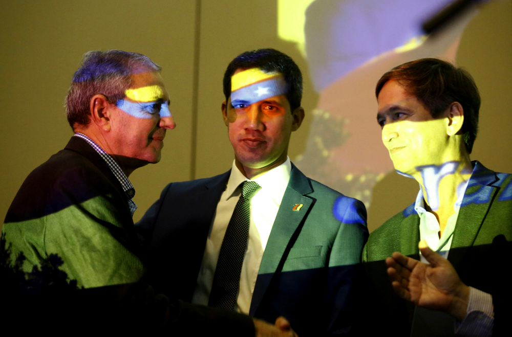 Venezuela's opposition leader and self-proclaimed interim president Juan Guaido, center, speaks with members of the opposition in Carabobo State, Manuel Barreto, left, and Lucio Herrera, prior a speech during a meeting with supporters, at a hotel in Valencia, Venezuela, June 7, 2019. The colors on their faces are the colors of Venezuelan flag projected by a data projector. (AP Photo/Juan Carlos Hernandez) Venezuela's opposition leader and self-proclaimed interim president Juan Guaido, center, speaks with members of the opposition in Carabobo State, Manuel Barreto, left, and Lucio Herrera, prior a speech during a meeting with supporters, at a hotel in Valencia, Venezuela, June 7, 2019. The colors on their faces are the colors of Venezuelan flag projected by a data projector. (AP Photo/Juan Carlos Hernandez)