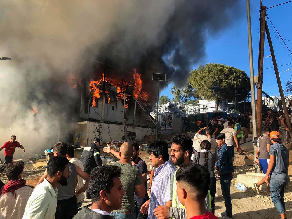 Migrants and refugees stand next to burning house containers at the Moria refugee camp, on the northeastern Aegean island of Lesbos, Greece, Sunday, Sept. 29, 2019. Migrants protesting at an overcrowded camp on the Greek island of Lesbos set fires and clashed with police Sunday, authorities said. Police and local authorities said there were unconfirmed reports of two fatalities at the Moria camp. (InTime News via AP) Migrants and refugees stand next to burning house containers at the Moria refugee camp, on the northeastern Aegean island of Lesbos, Greece, Sunday, Sept. 29, 2019. Migrants protesting at an overcrowded camp on the Greek island of Lesbos set fires and clashed with police Sunday, authorities said. Police and local authorities said there were unconfirmed reports of two fatalities at the Moria camp. (InTime News via AP)