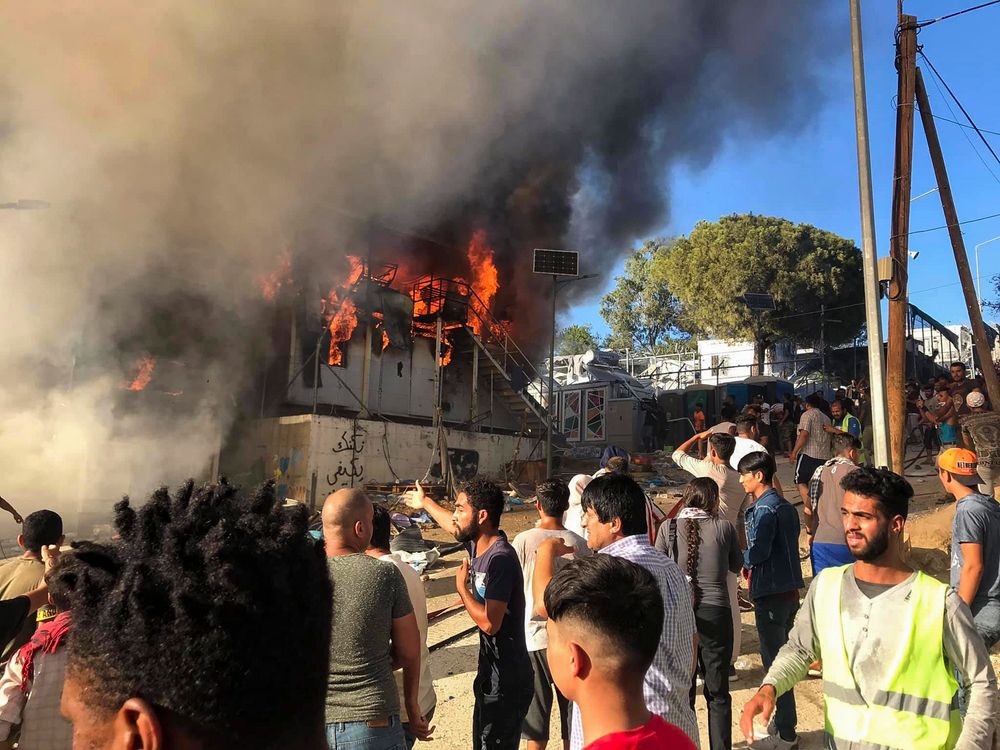Migrants and refugees stand next to burning house containers at the Moria refugee camp, on the northeastern Aegean island of Lesbos, Greece, Sunday, Sept. 29, 2019. Migrants protesting at an overcrowded camp on the Greek island of Lesbos set fires and clashed with police Sunday, authorities said. Police and local authorities said there were unconfirmed reports of two fatalities at the Moria camp. (InTime News via AP) Migrants and refugees stand next to burning house containers at the Moria refugee camp, on the northeastern Aegean island of Lesbos, Greece, Sunday, Sept. 29, 2019. Migrants protesting at an overcrowded camp on the Greek island of Lesbos set fires and clashed with police Sunday, authorities said. Police and local authorities said there were unconfirmed reports of two fatalities at the Moria camp. (InTime News via AP)