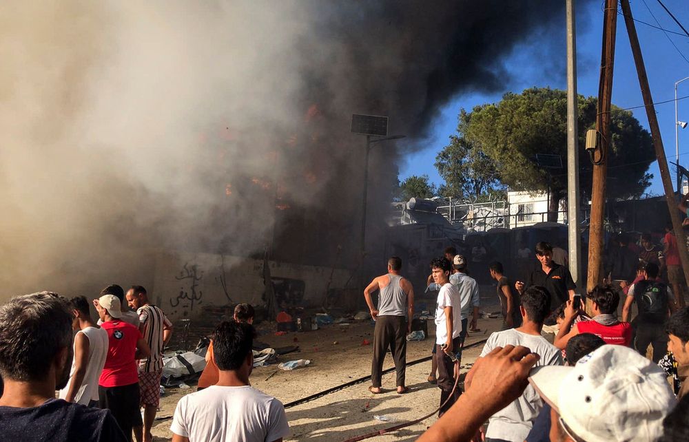 Migrants and refugees stand next to burning house containers at the Moria refugee camp, on the northeastern Aegean island of Lesbos, Greece, Sunday, Sept. 29, 2019. Migrants protesting at an overcrowded camp on the Greek island of Lesbos set fires and clashed with police Sunday, authorities said. Police and local authorities said there were unconfirmed reports of two fatalities at the Moria camp. (InTime News via AP) Migrants and refugees stand next to burning house containers at the Moria refugee camp, on the northeastern Aegean island of Lesbos, Greece, Sunday, Sept. 29, 2019. Migrants protesting at an overcrowded camp on the Greek island of Lesbos set fires and clashed with police Sunday, authorities said. Police and local authorities said there were unconfirmed reports of two fatalities at the Moria camp. (InTime News via AP)
