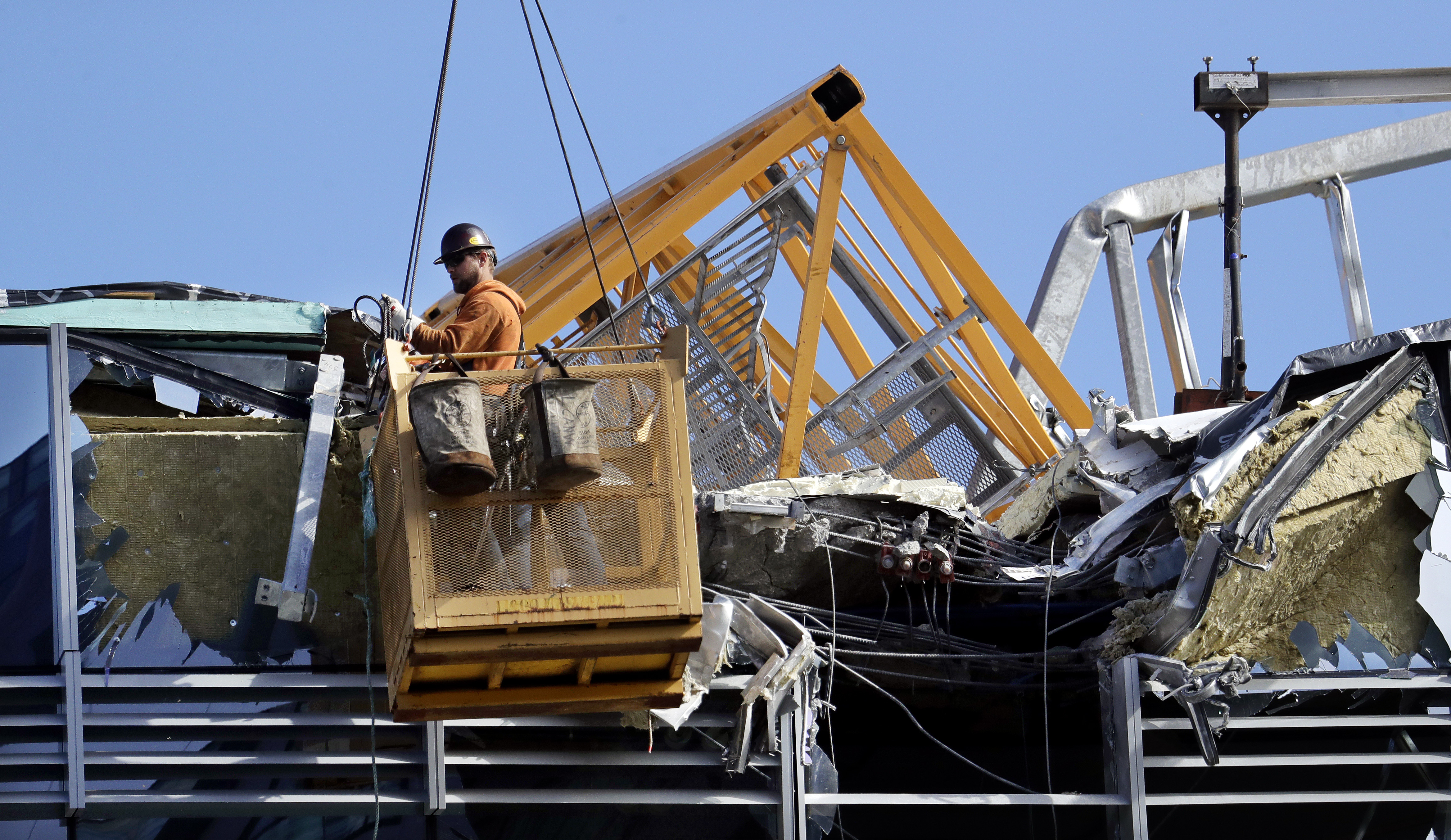 With a portion of the broken crane on the roof behind, a worker suspended in a basket clears debris from a building damaged when the crane atop it collapsed a day earlier, Sunday, April 28, 2019, in Seattle. The construction crane fell from a building on Google's new campus during a storm that brought wind gusts, crashing down onto one of the city's busiest streets and killing multiple people. (AP Photo/Elaine Thompson) With a portion of the broken crane on the roof behind, a worker suspended in a basket clears debris from a building damaged when the crane atop it collapsed a day earlier, Sunday, April 28, 2019, in Seattle. The construction crane fell from a building on Google's new campus during a storm that brought wind gusts, crashing down onto one of the city's busiest streets and killing multiple people. (AP Photo/Elaine Thompson)