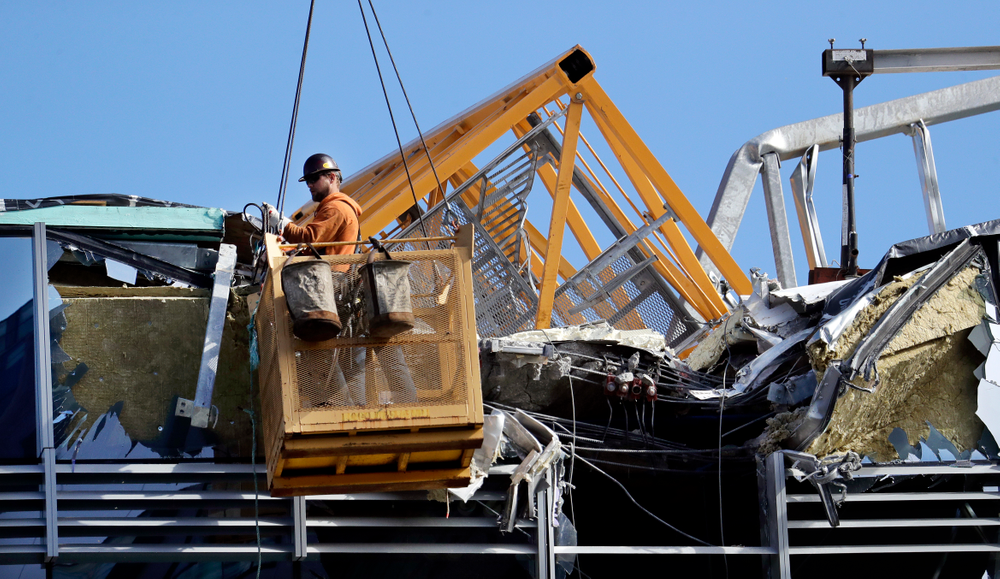 With a portion of the broken crane on the roof behind, a worker suspended in a basket clears debris from a building damaged when the crane atop it collapsed a day earlier, Sunday, April 28, 2019, in Seattle. The construction crane fell from a building on Google's new campus during a storm that brought wind gusts, crashing down onto one of the city's busiest streets and killing multiple people. (AP Photo/Elaine Thompson) With a portion of the broken crane on the roof behind, a worker suspended in a basket clears debris from a building damaged when the crane atop it collapsed a day earlier, Sunday, April 28, 2019, in Seattle. The construction crane fell from a building on Google's new campus during a storm that brought wind gusts, crashing down onto one of the city's busiest streets and killing multiple people. (AP Photo/Elaine Thompson)